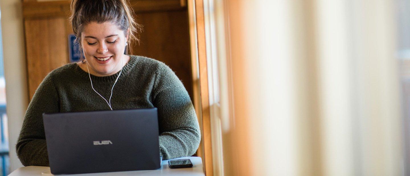 woman with headphones, seated with an open laptop